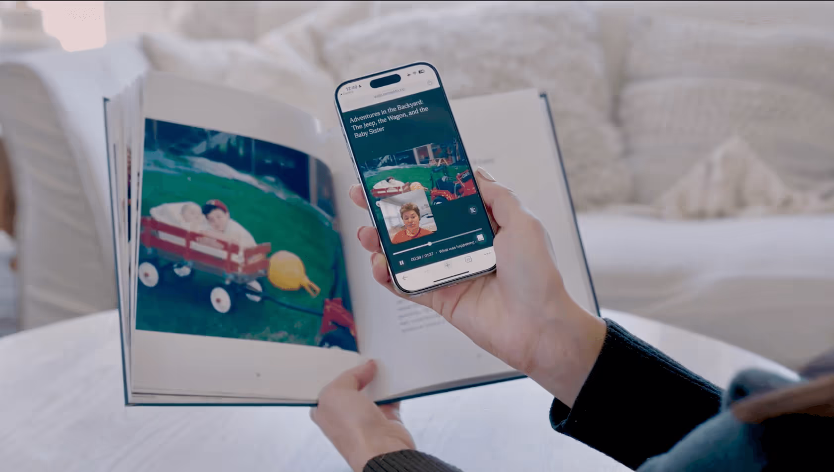 A person is holding a phone in front of the QR code printed inside a Remento hard-cover book. The phone shows the same story with the original video on Remento