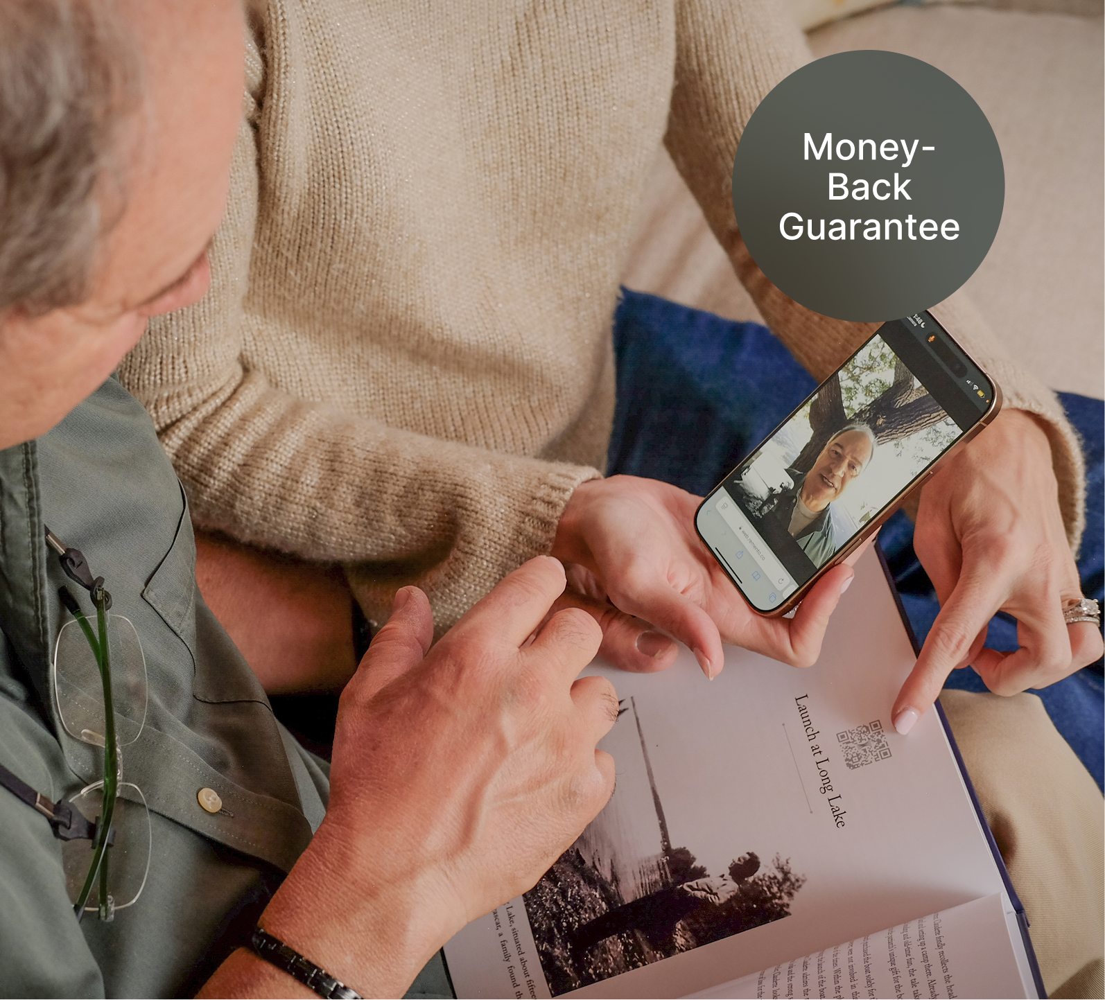 A photo of 2 people holding a phone and watching a story on Remento. The phone is held above the corresponding story printed in a Remento book