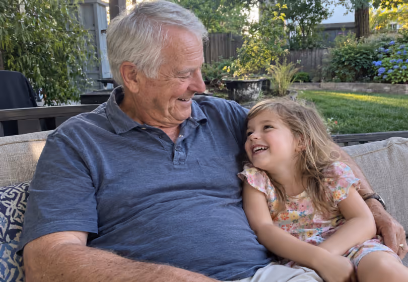 Grandfather laughing with his granddaughter on a patio couch