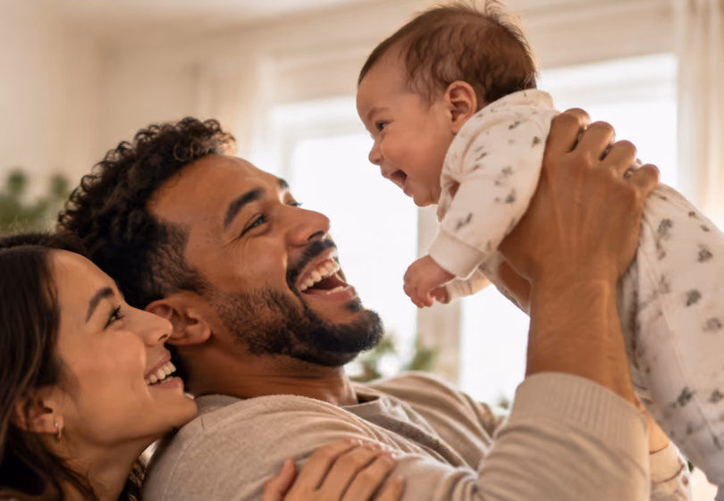 Laughing dad lifting his baby overhead as mom smiles beside him