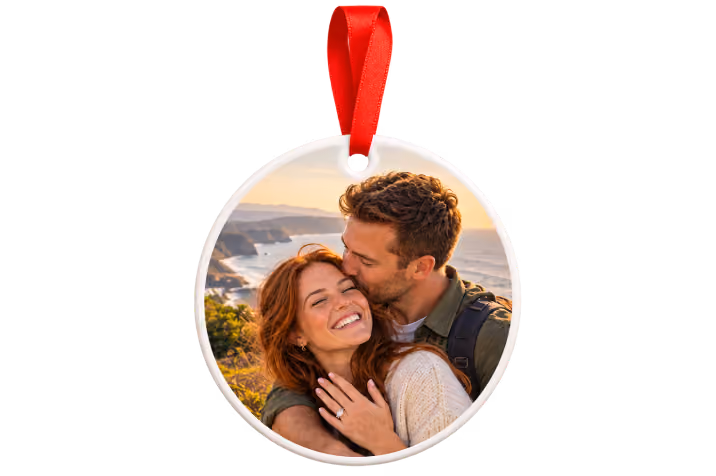 Ceramic engagement photo ornament with red ribbon showing a man kissing his smiling fiancee