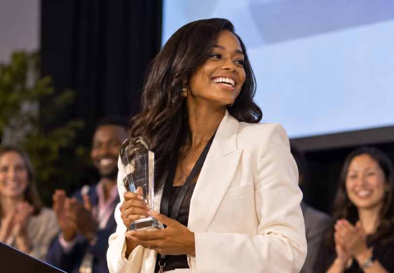 Woman holding an award on stage as colleagues applaud