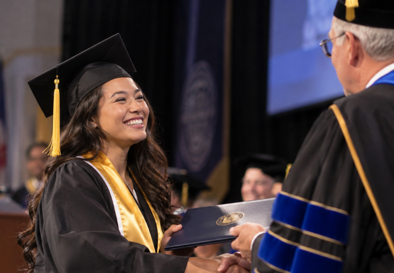 Graduate in cap and gown smiling as she receives her diploma on stage