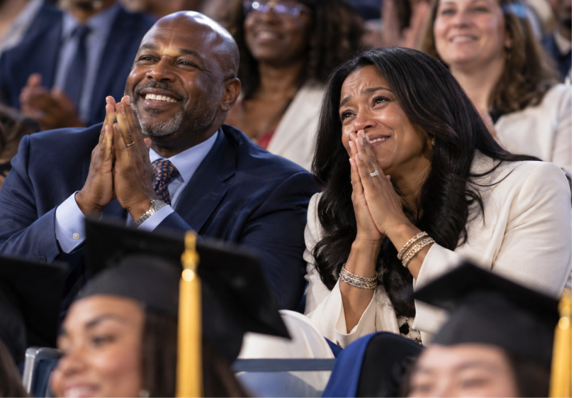 Proud parents clapping and tearing up in the audience at a graduation ceremony